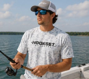Angler wearing Hookset Outdoors Blue Ice camouflage short sleeve performance fishing shirt while fishing from a boat on a sunny day.