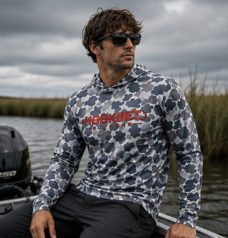 Man wearing Hookset Storm Grey UPF 50 fishing hoodie sitting on a boat in marsh water.
